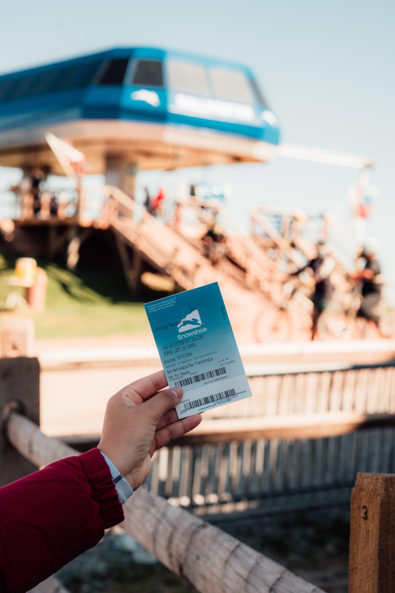 A lift ticket held up at the Ballhooter base with riders loading behind it