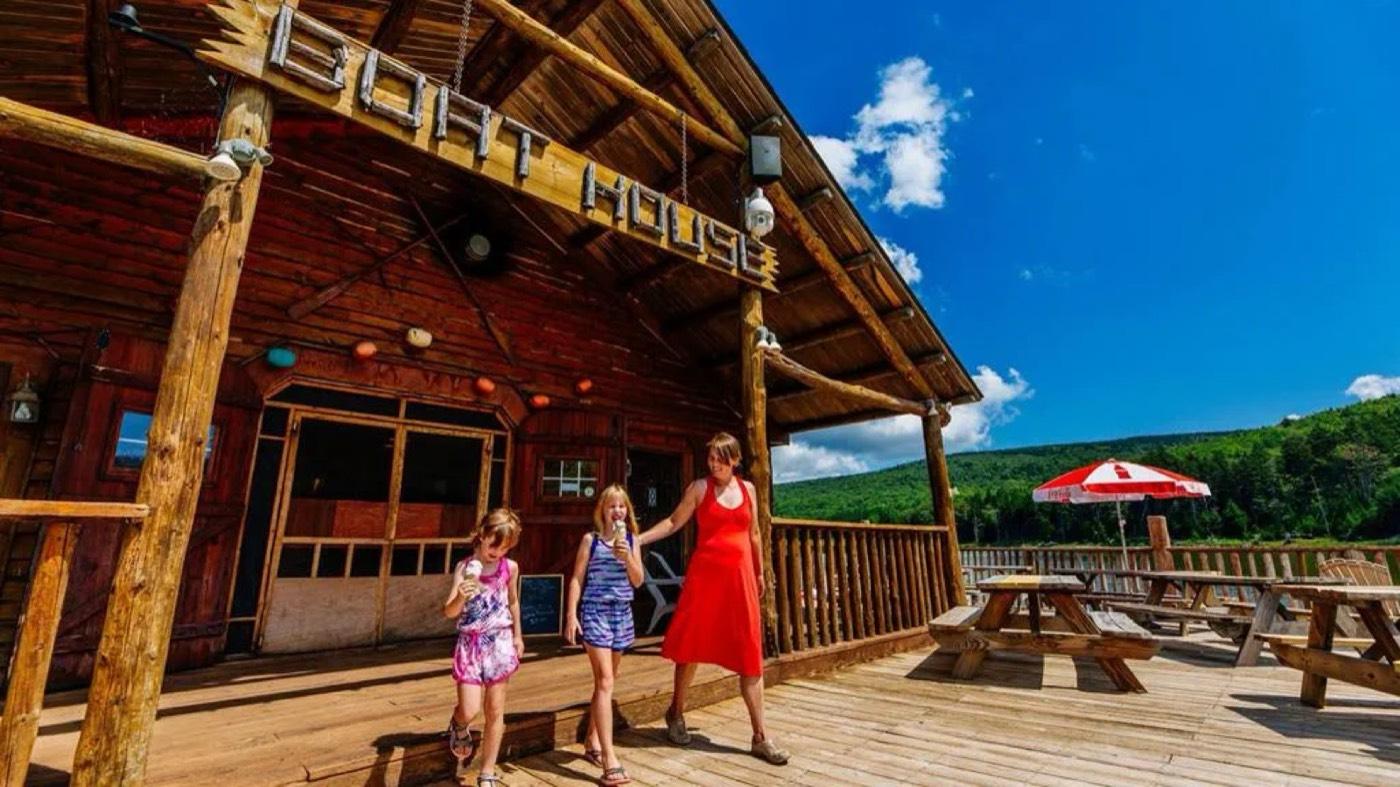 The Boathouse deck at Shavers Lake on a blue-sky summer day, a family walking past the picnic tables