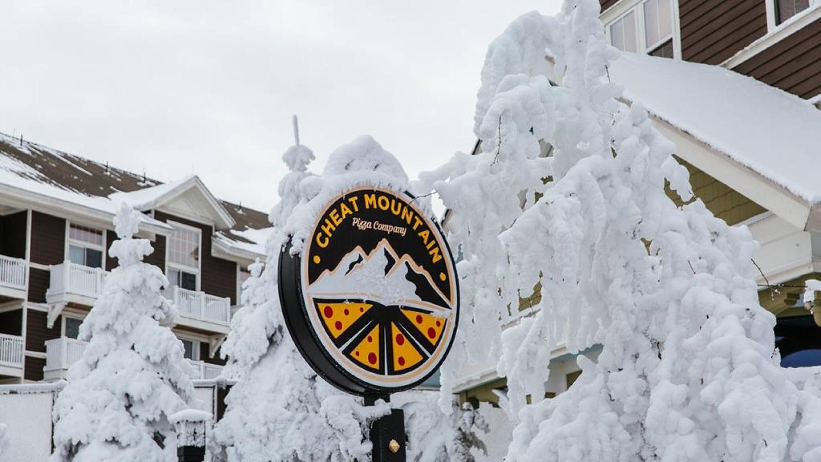 The Cheat Mountain Pizza sign in the Village after a heavy snow, the trees behind it coated white