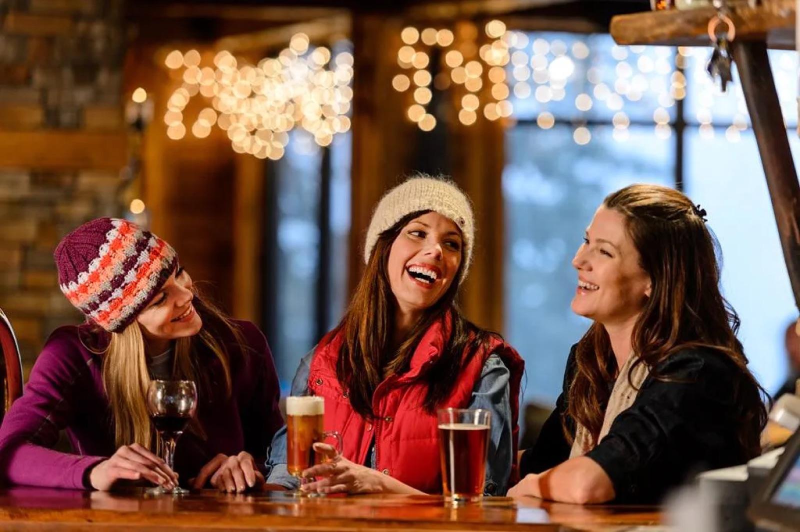 Three friends laughing over drinks at the Foxfire Grille bar with the mountain view behind them