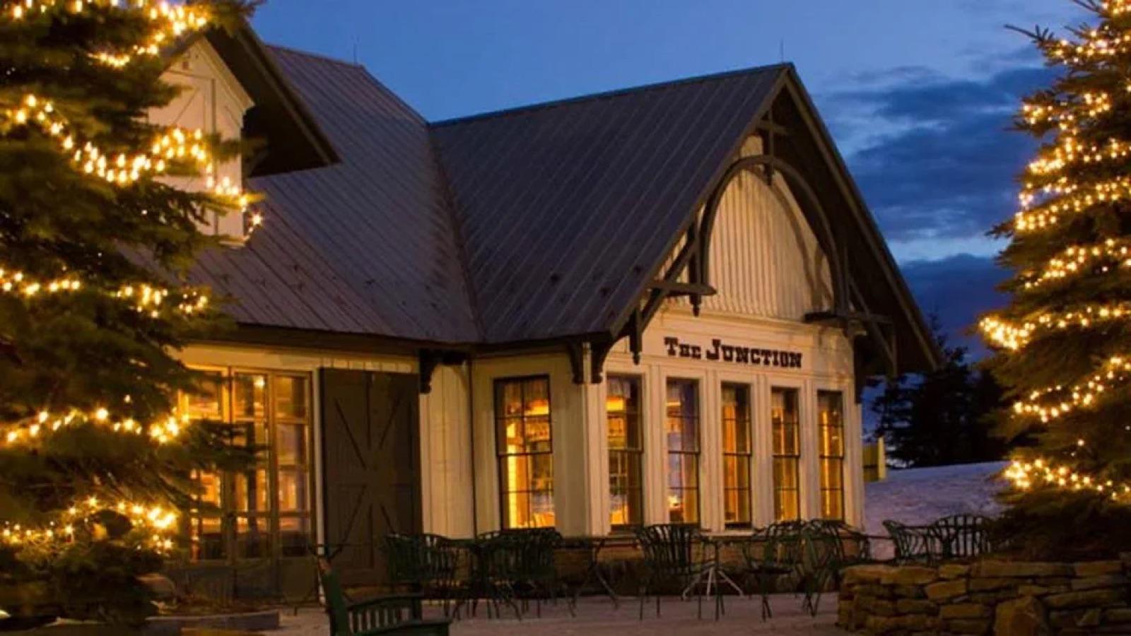 The Junction Ale House at dusk in winter with string lights on the spruce trees out front
