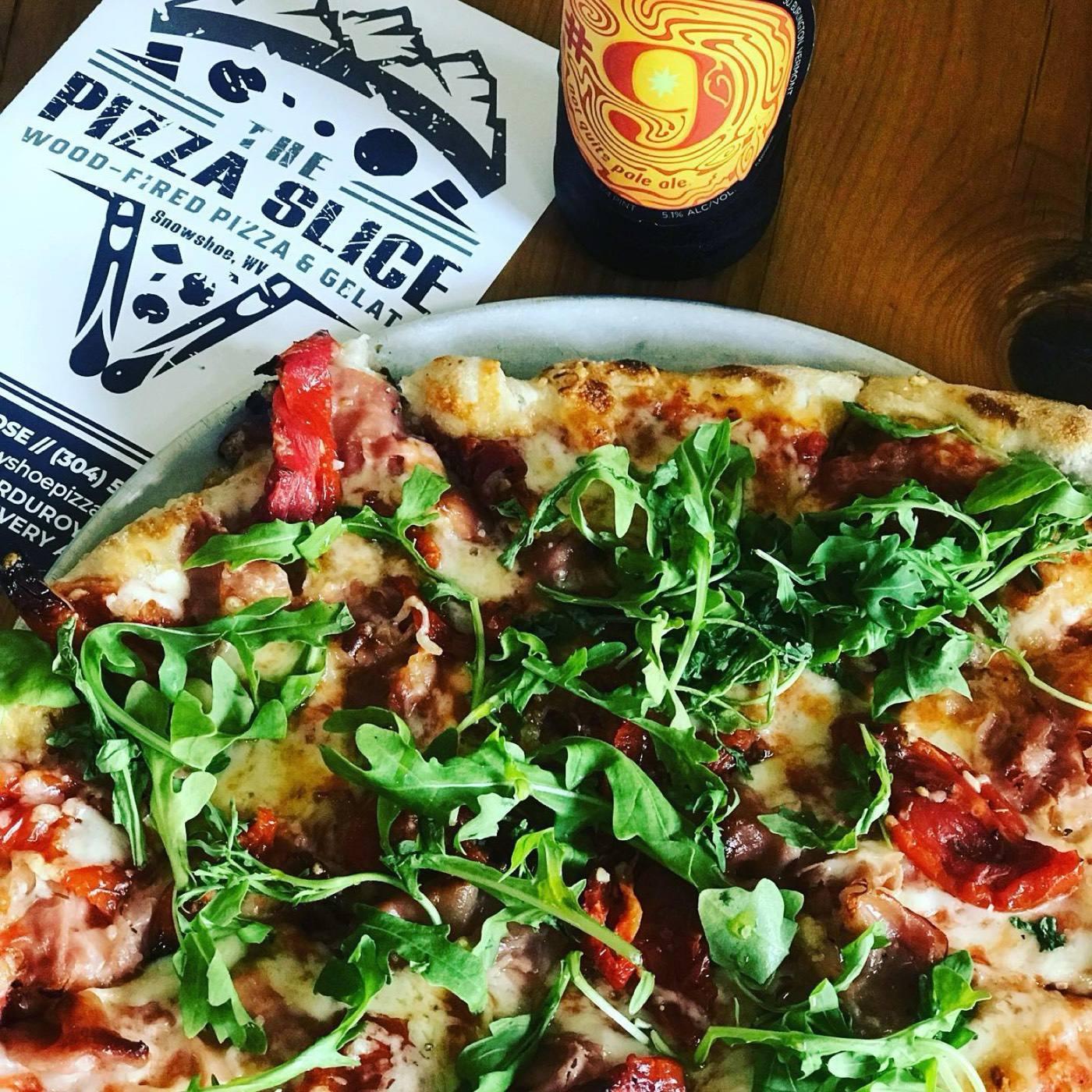 A wood-fired pizza topped with arugula and prosciutto at The Pizza Slice, menu and a bottle beside it