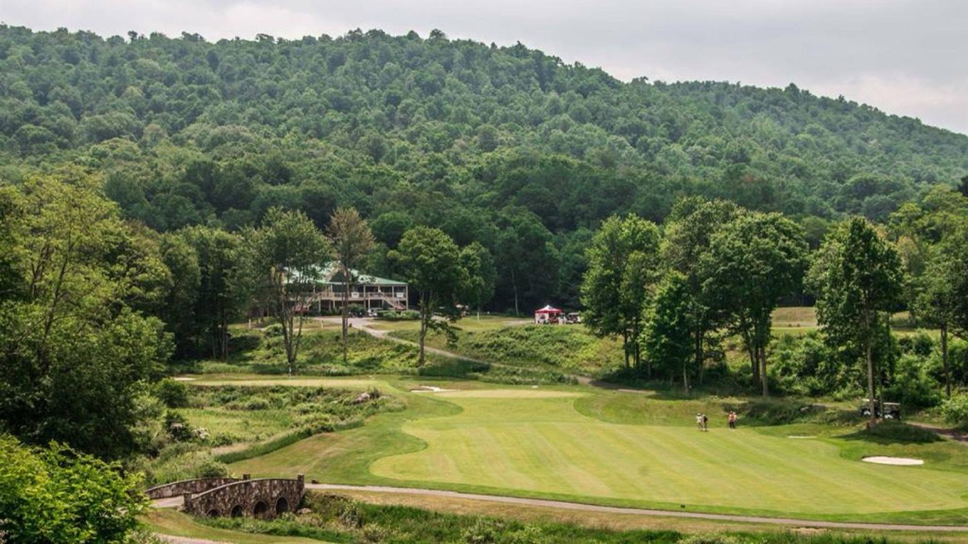 A green fairway at Raven Golf Club with the clubhouse and Raven Grille on the hill behind it in summer