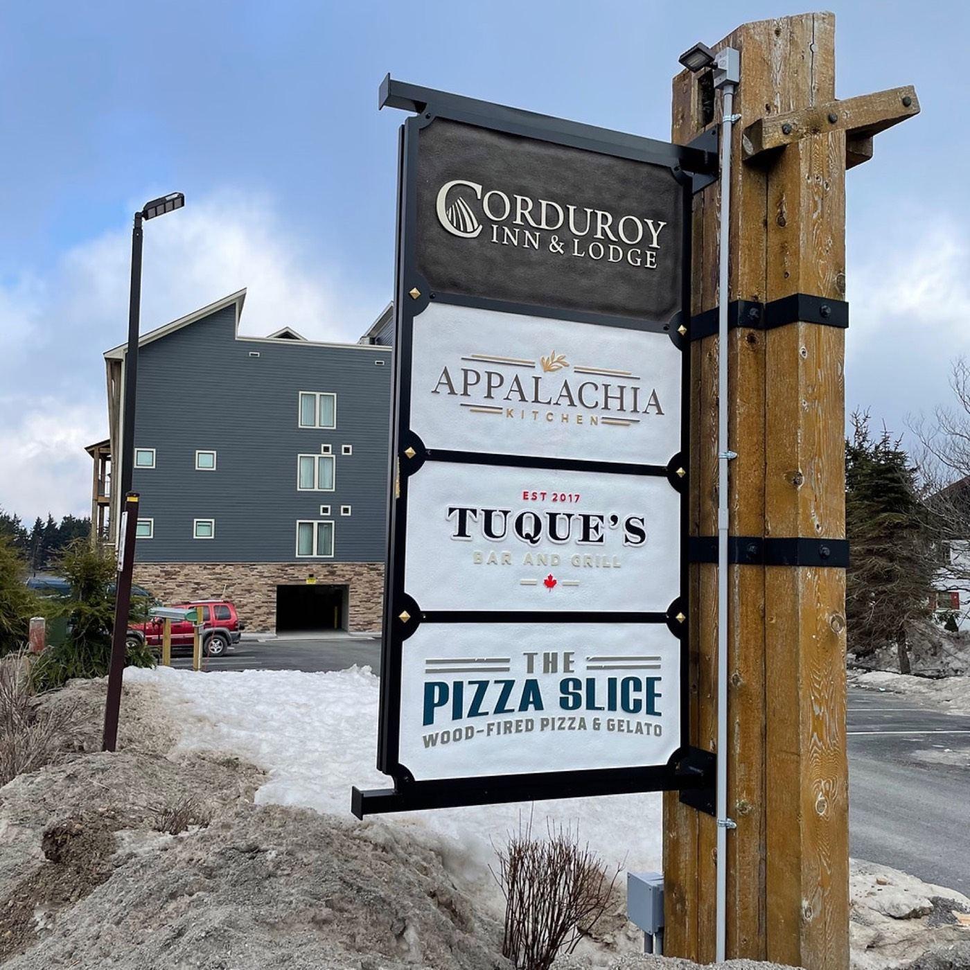The roadside sign for the Corduroy Inn, Appalachia Kitchen, Tuque's Bar and Grill, and The Pizza Slice in winter